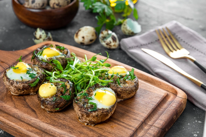 Sugerencia-de-presentacion-microgreens-baked-champignons-with-quail-eggs-microgreen-garnish-wooden-cutting-board-close-up